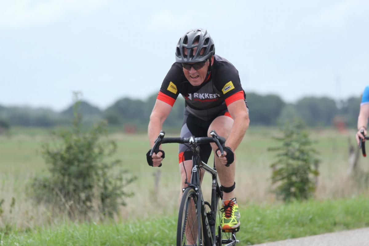 Een man met een helm rijdt op een fiets over de weg.