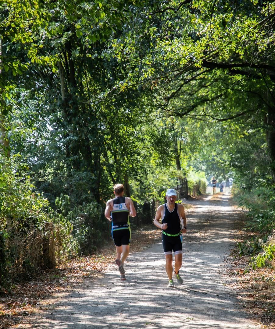 Twee mensen rennen over een zandpad in het bos.