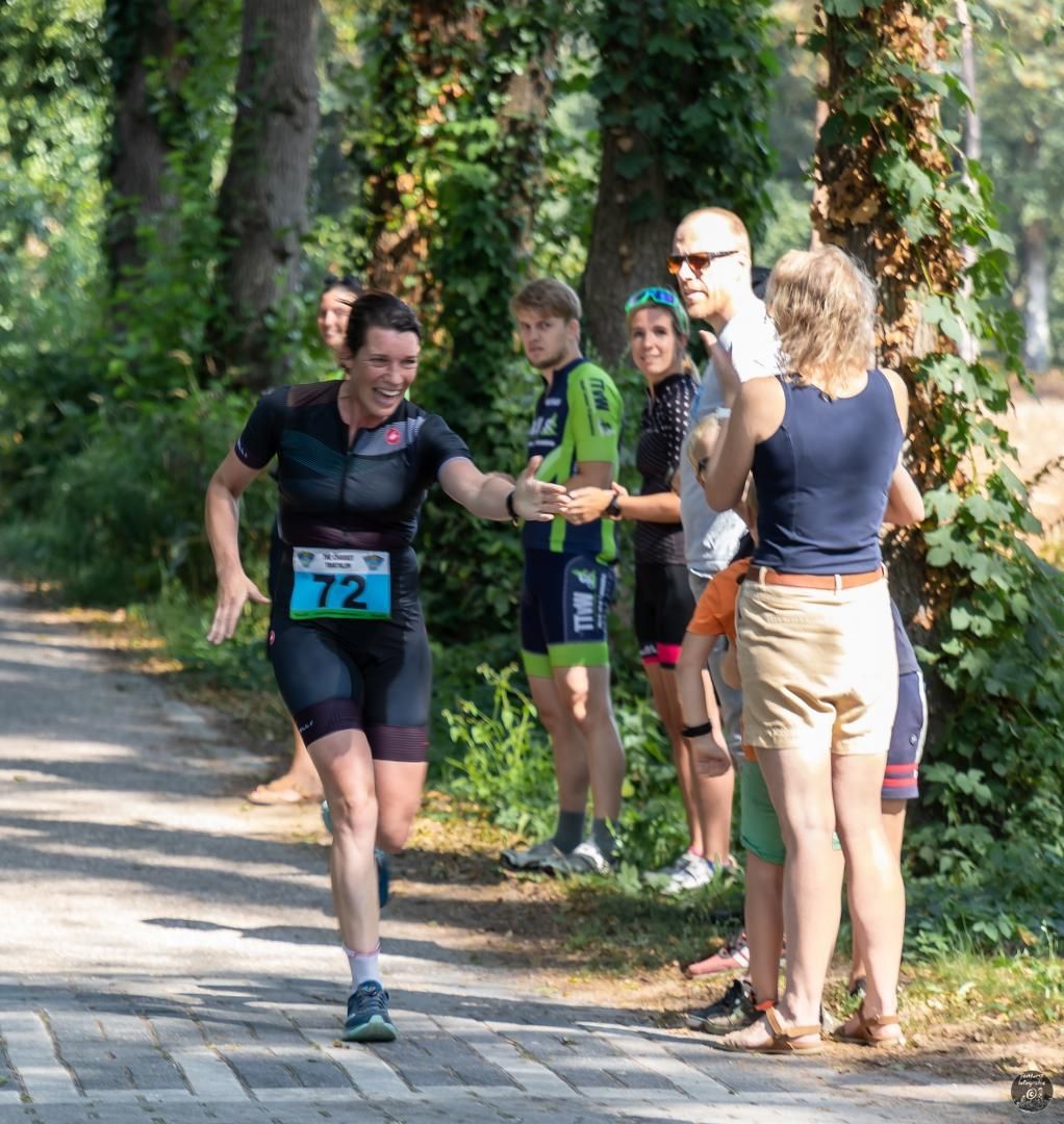 Een groep mensen staat langs de kant van de weg en kijkt naar een hardloper.