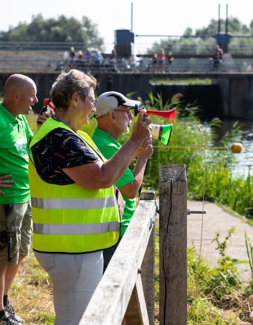 Een groep mensen in groene shirts en gele hesjes staat naast een houten hek.