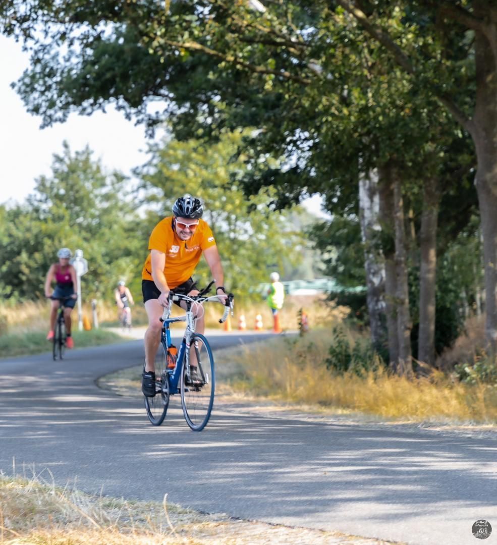 Een man in een oranje shirt fietst over een weg