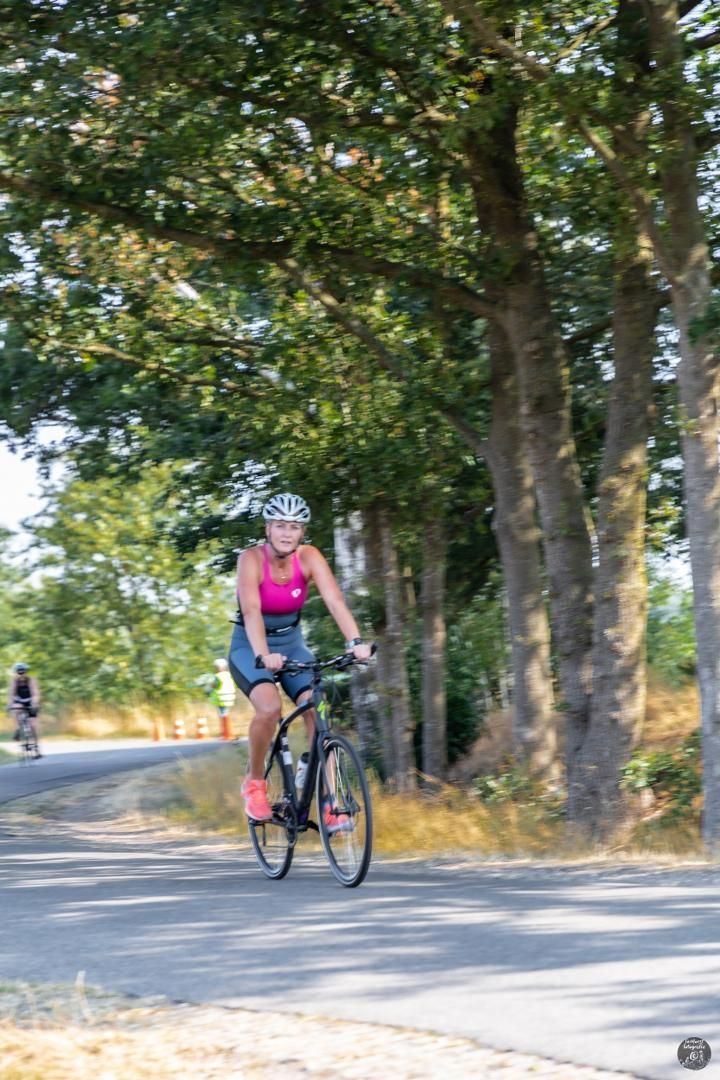 Een vrouw fietst over een weg die omgeven is door bomen.