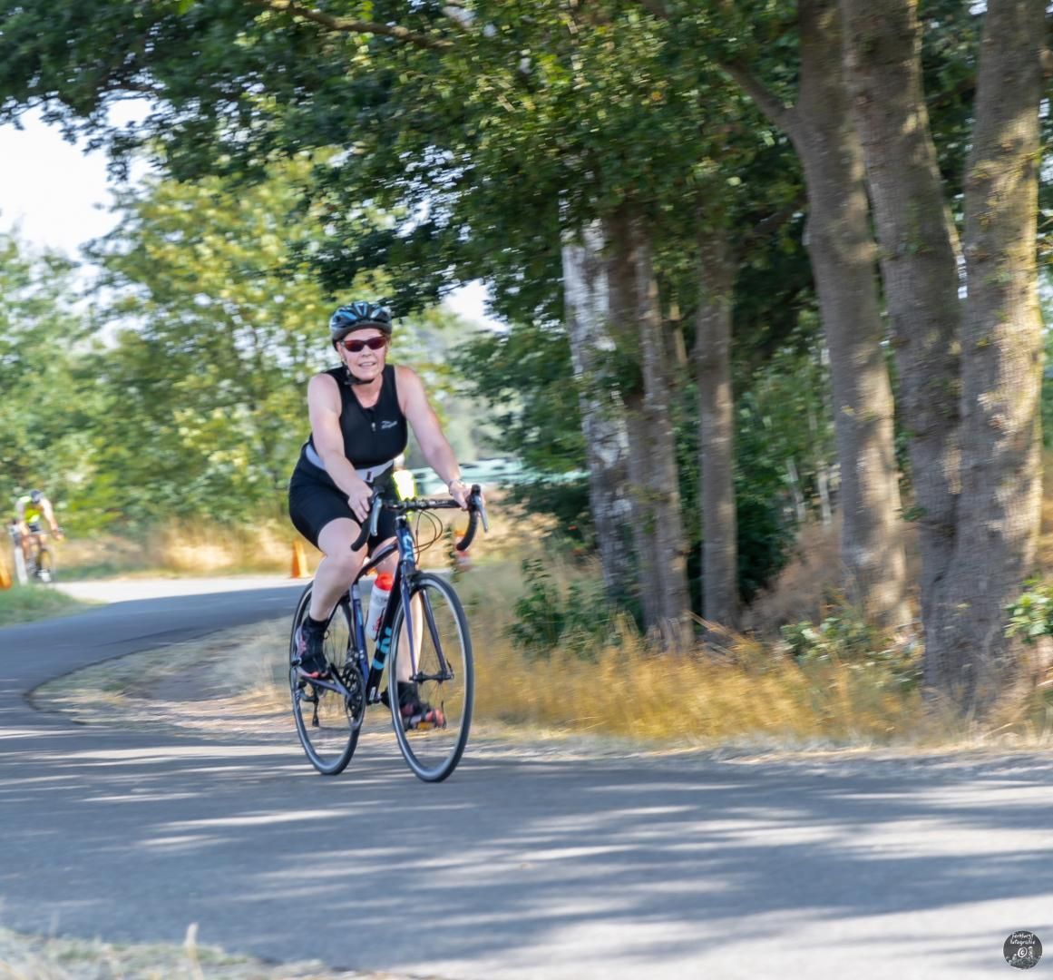 Een vrouw fietst over een weg met bomen op de achtergrond
