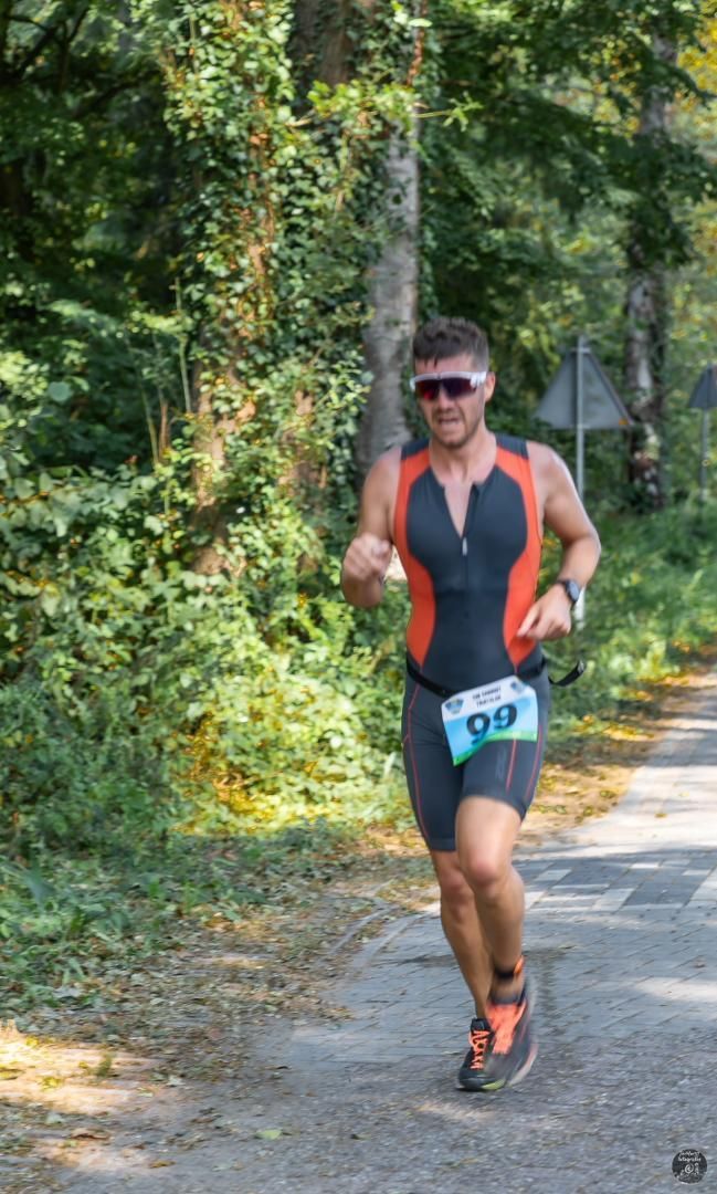 Een man in een triatlonpak rent over de weg.