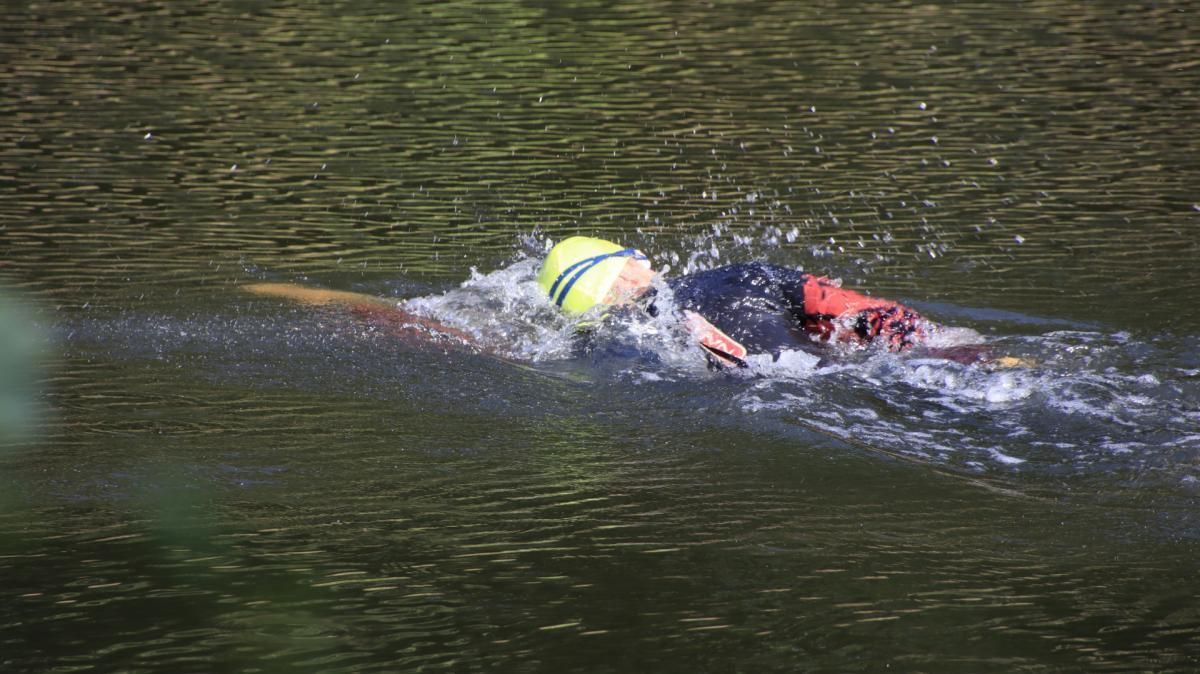 Iemand zwemt in een meer met een gele bal.