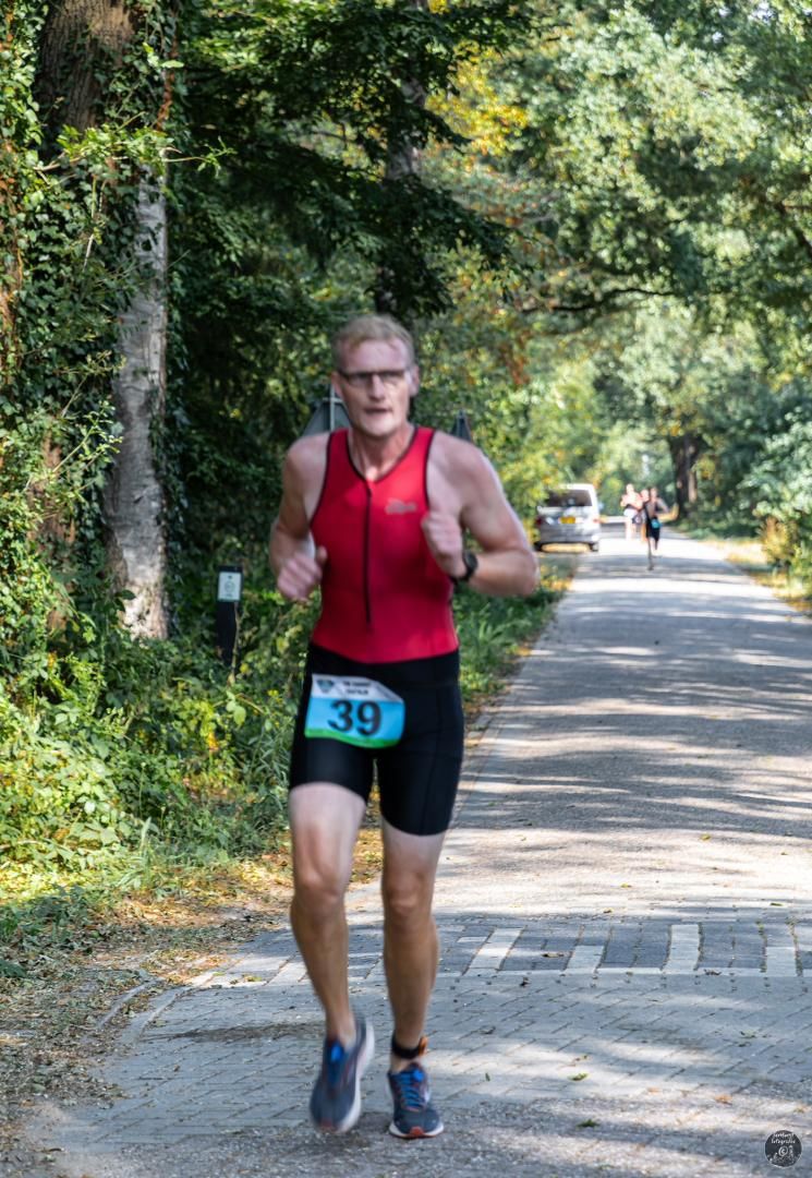 Een man in een rood shirt en een zwarte korte broek rent over de weg.