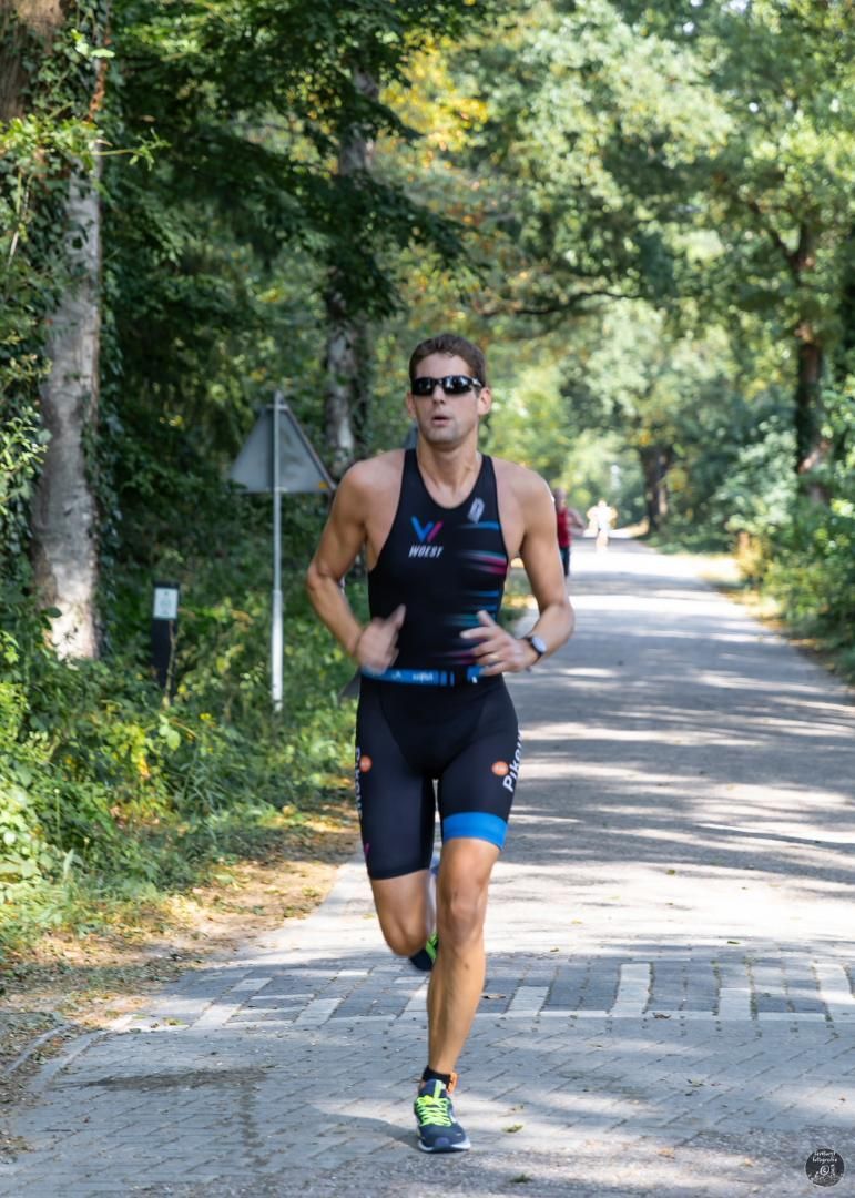 Een man rent over een weg die omgeven is door bomen.