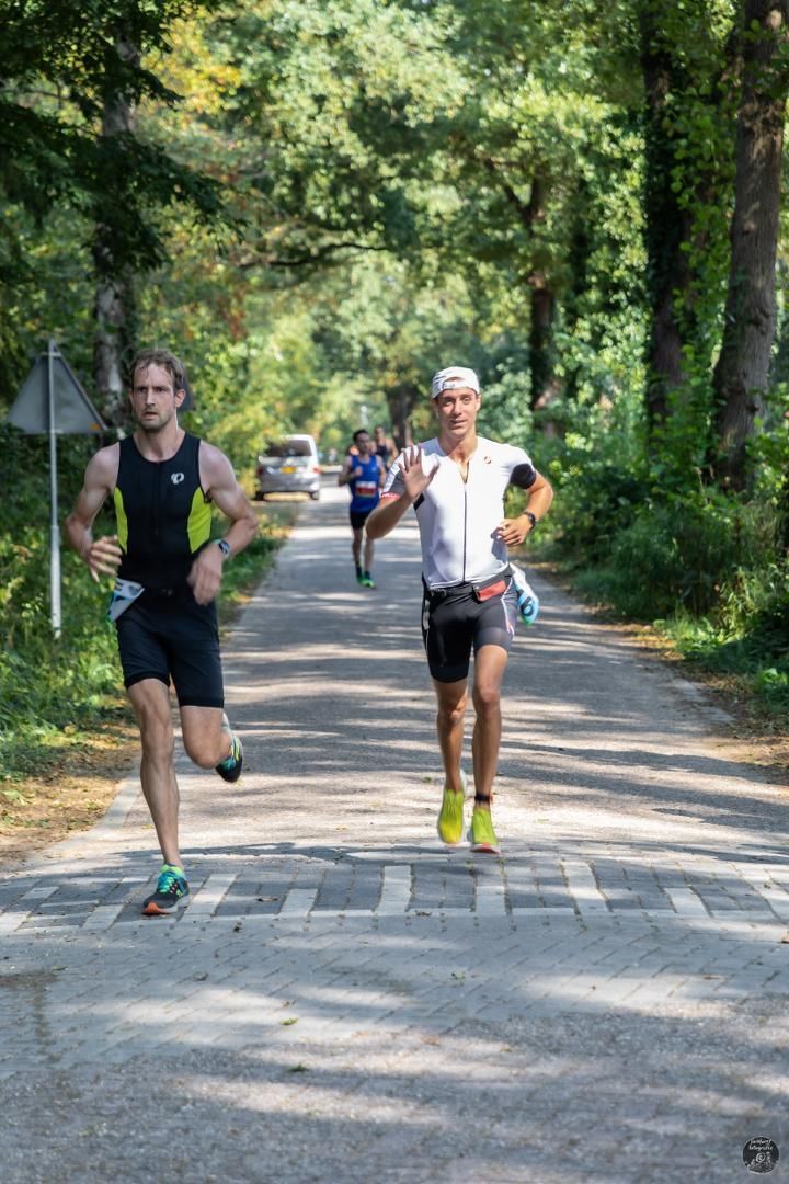 Twee mannen rennen over een weg in het bos.