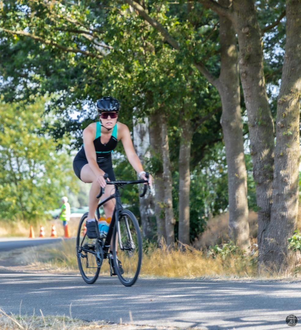 Een vrouw fietst over een weg met bomen op de achtergrond