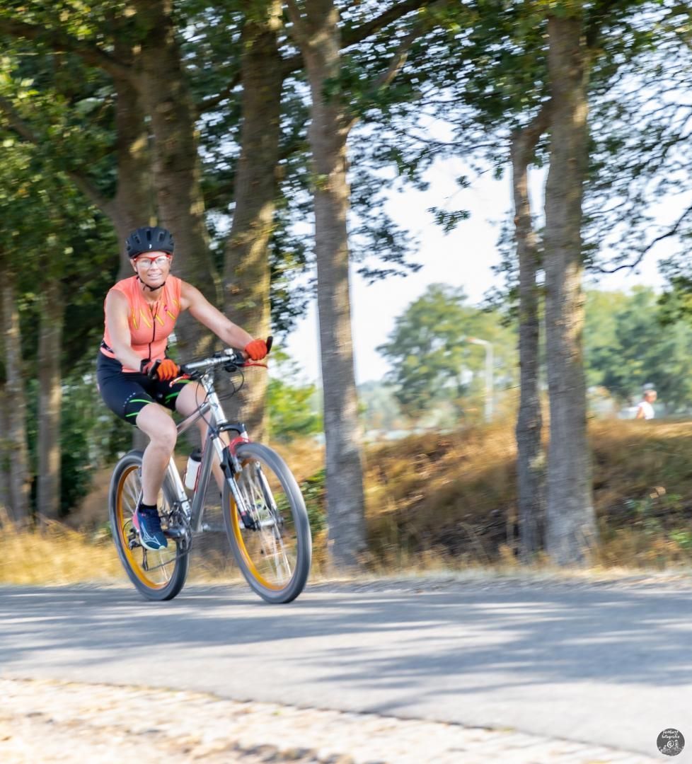 Een man fietst over een weg met bomen op de achtergrond.