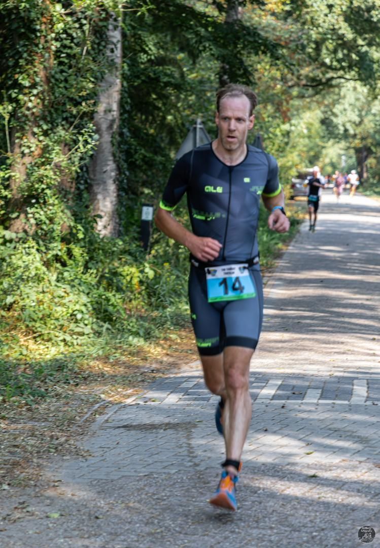 Een man in een triatlonpak rent over de weg.