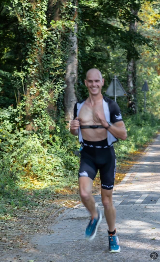 Een man zonder shirt rent over een weg in het bos.