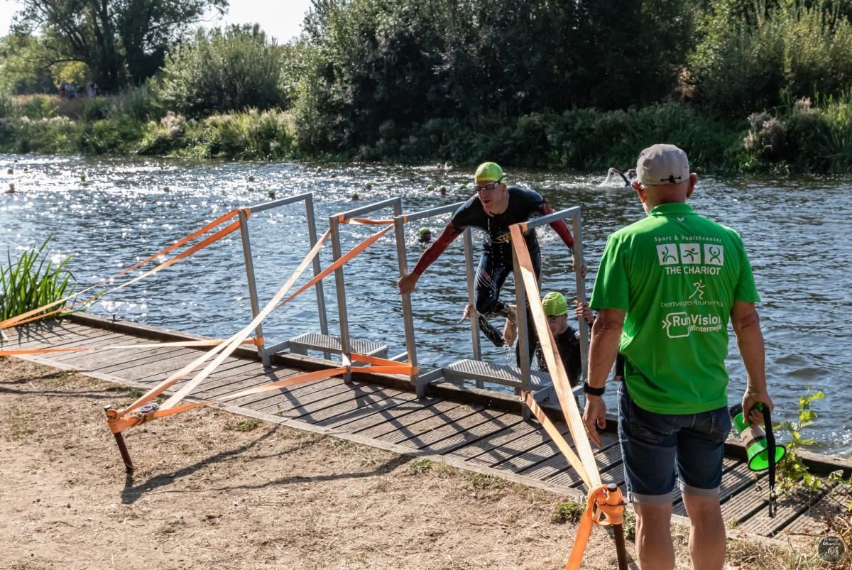 Een man in een groen shirt helpt een man om een ​​brug over een rivier over te steken.