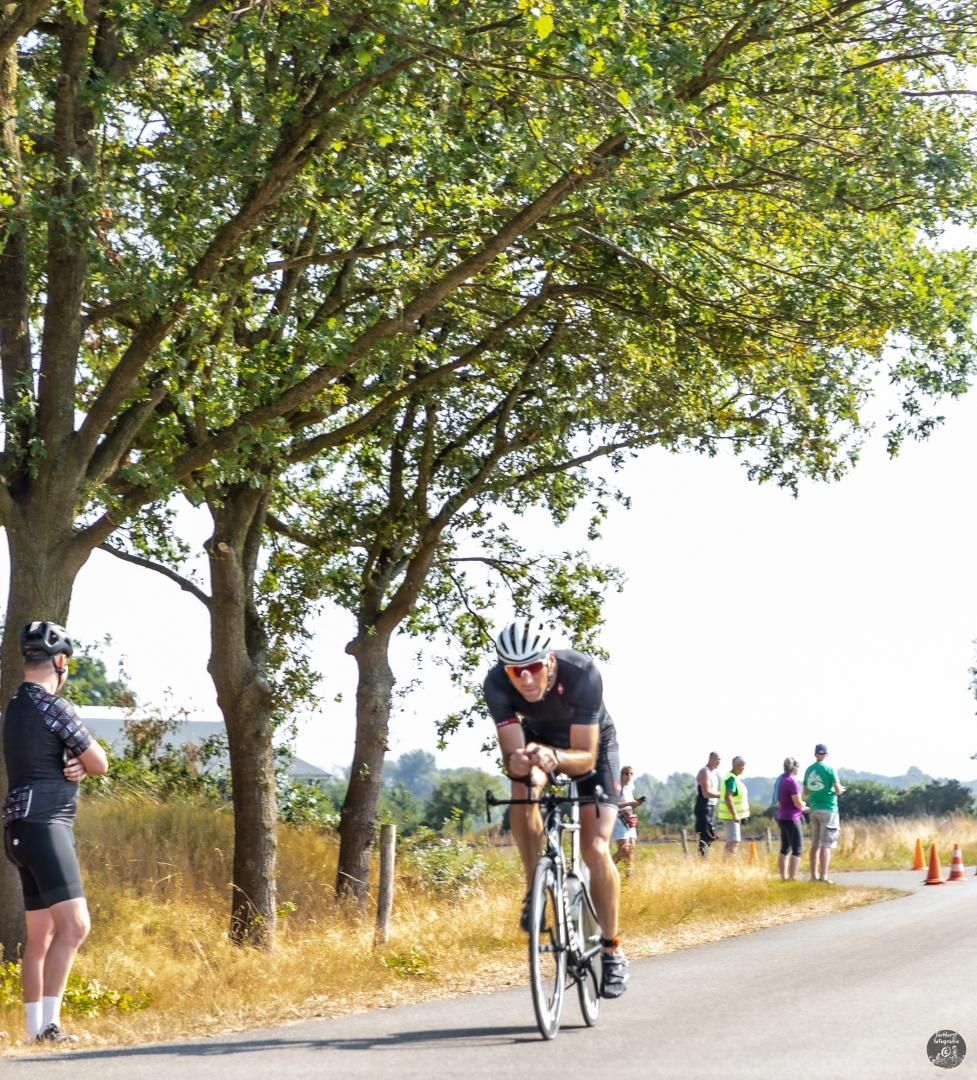 Een man die op een fiets over een weg rijdt met bomen op de achtergrond