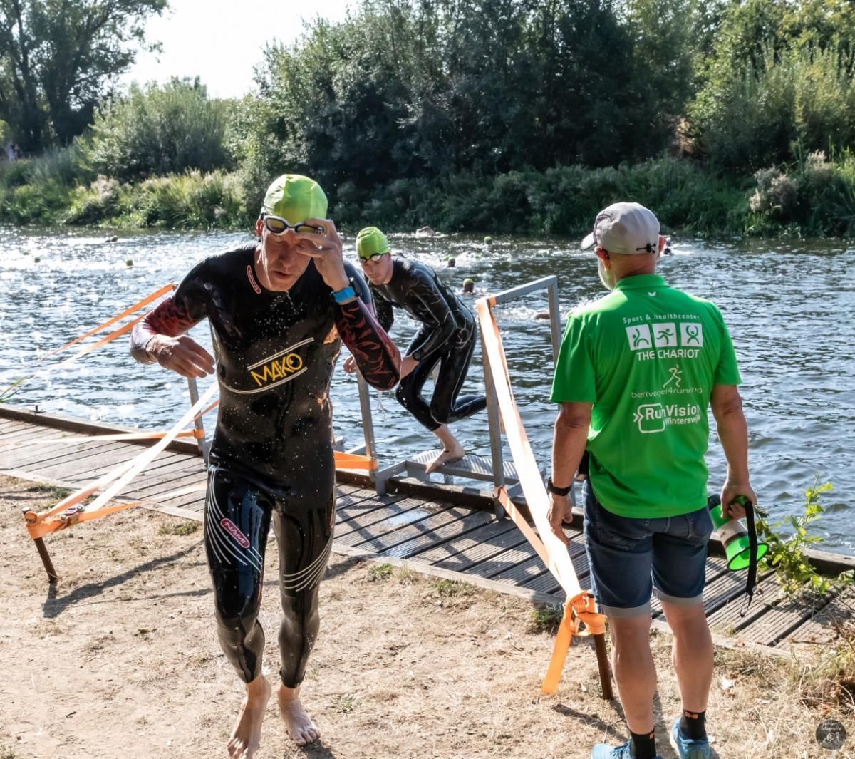 Een man in een groen shirt staat naast een man in een wetsuit.