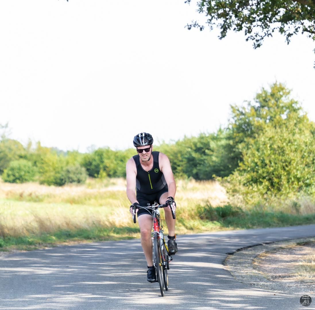 Een man met een helm en een zonnebril rijdt op een fiets over een weg