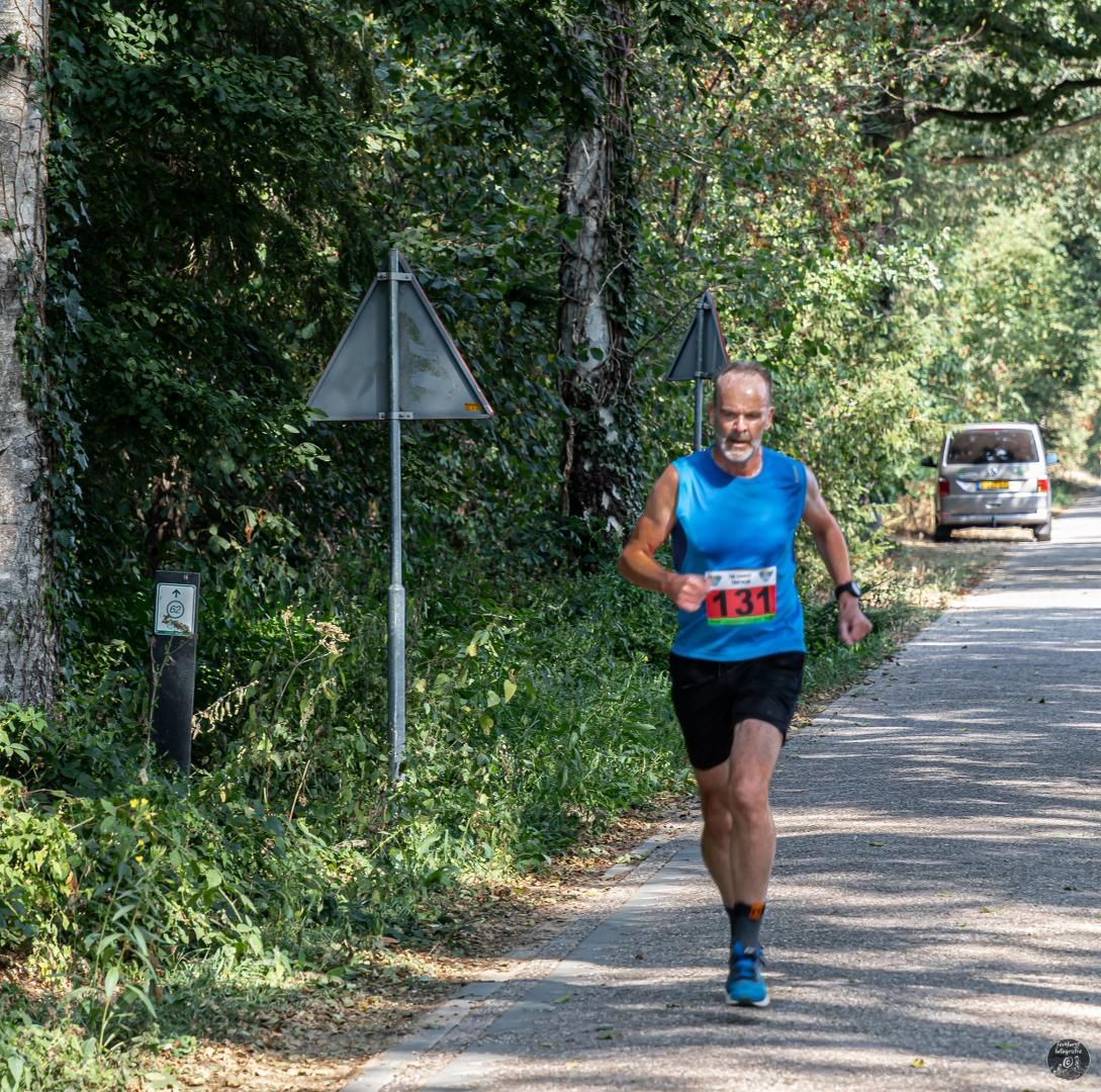 Een man in een blauw shirt rent over de weg.