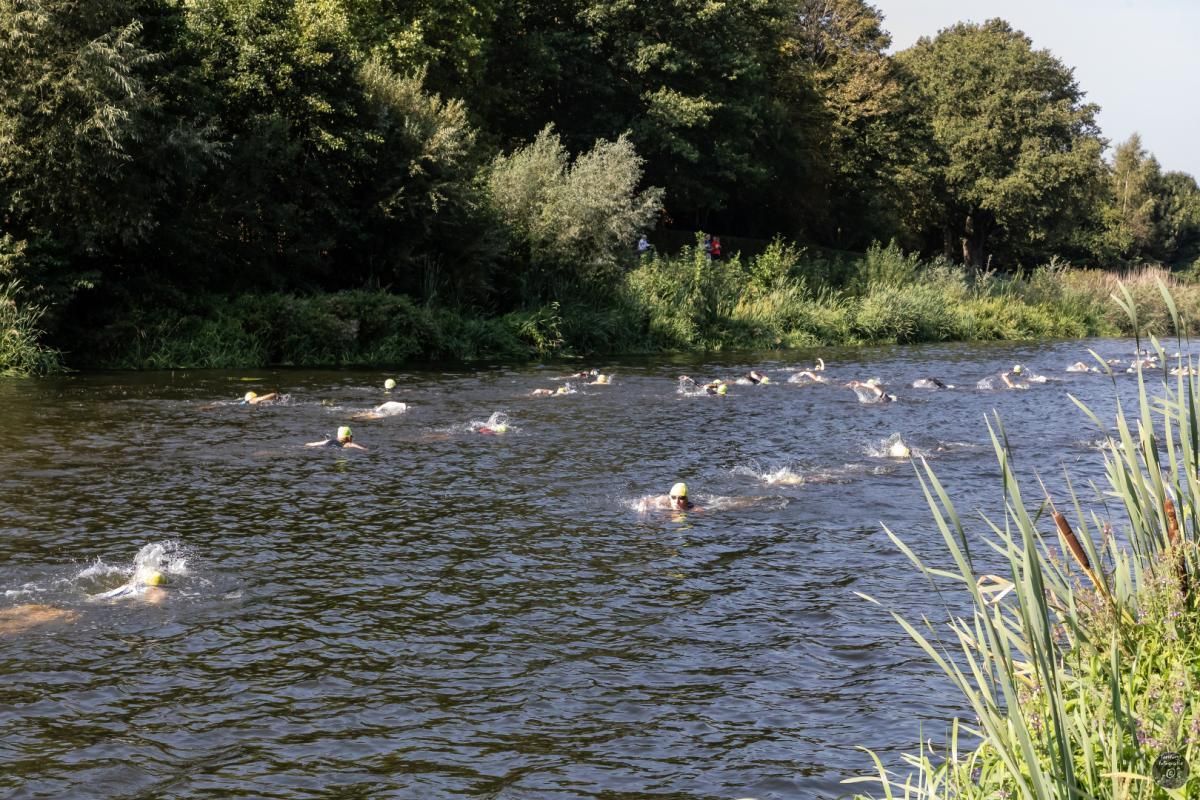 Een groep mensen zwemt in een rivier, omgeven door bomen.