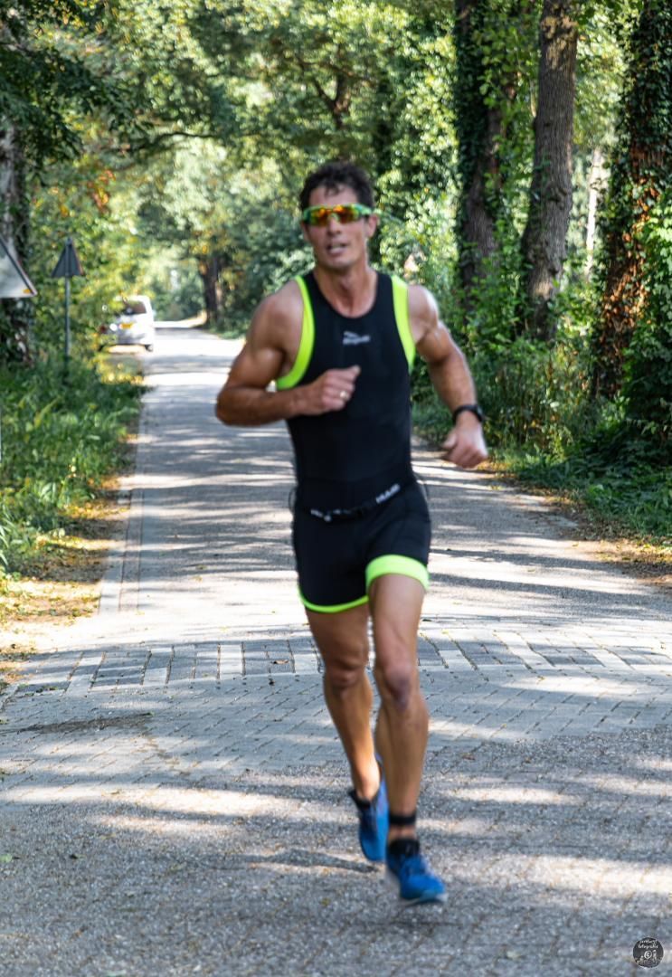 Een man rent over een weg met bomen op de achtergrond.