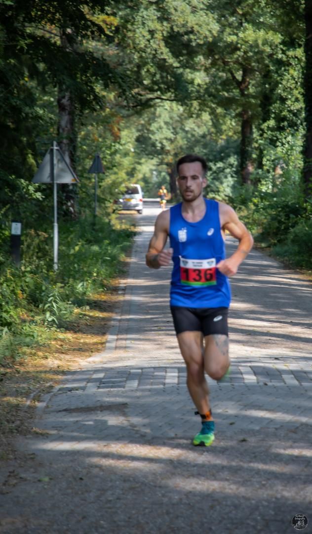 Een man rent over een weg in het bos.