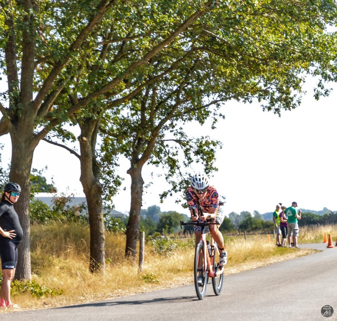 Een man die op een fiets over een weg rijdt met bomen op de achtergrond