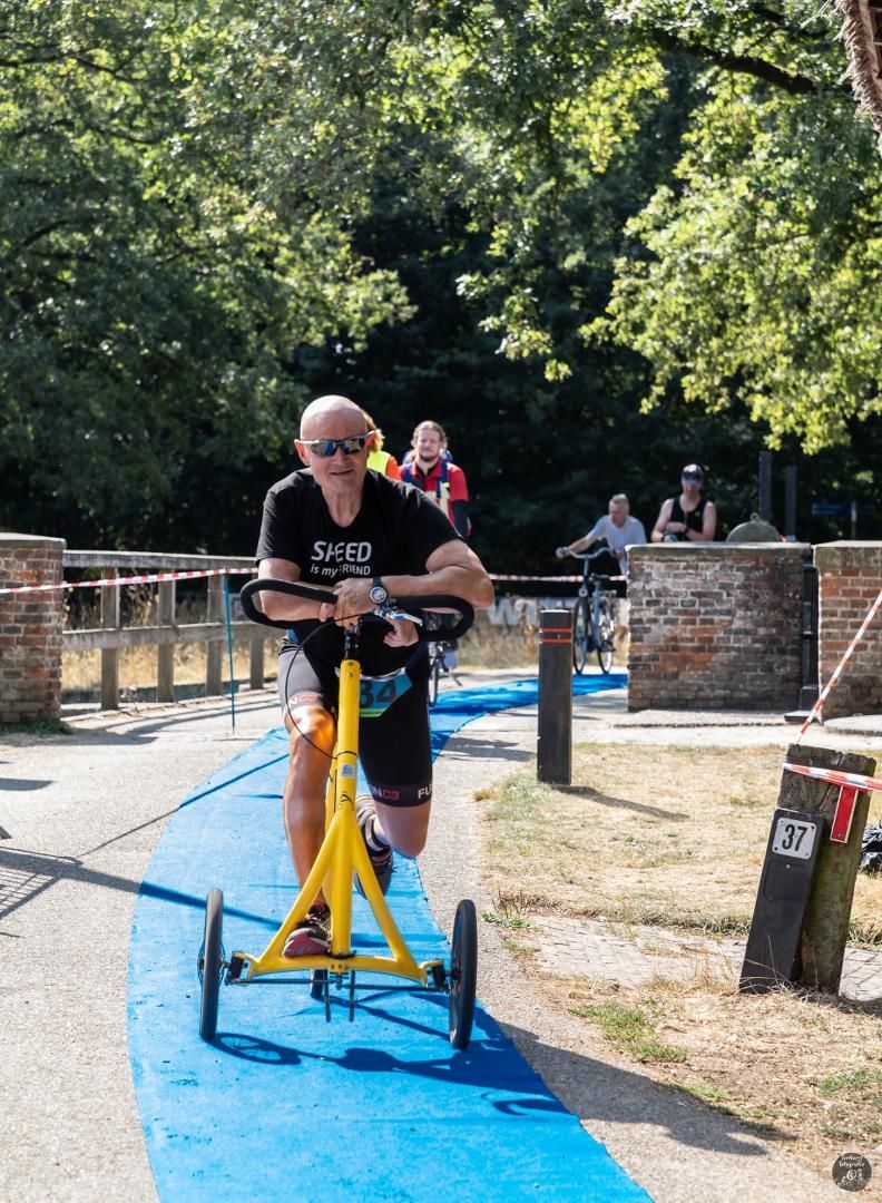 Een man rijdt op een gele driewieler op een blauw pad.