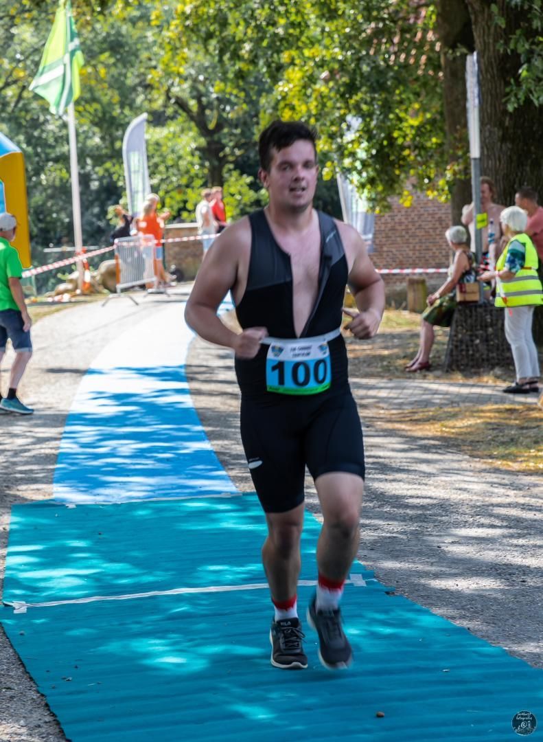 Een man doet mee aan een wedstrijd met het nummer 100 op zijn startnummer.