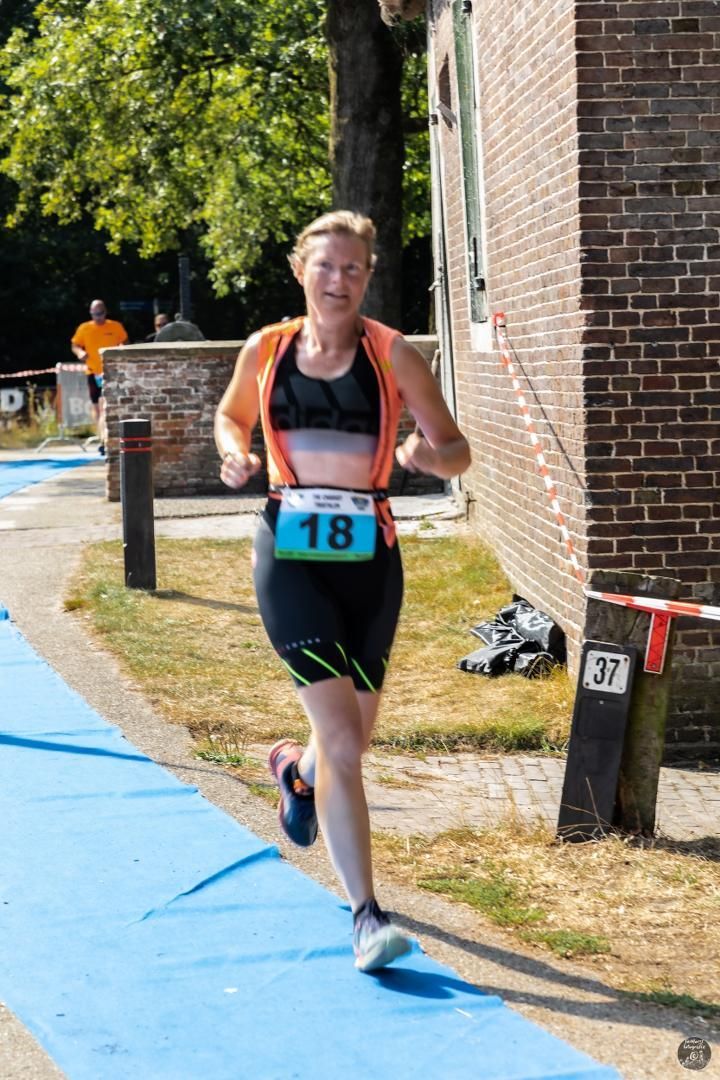 Een vrouw rent op een blauw tapijt voor een bakstenen gebouw.