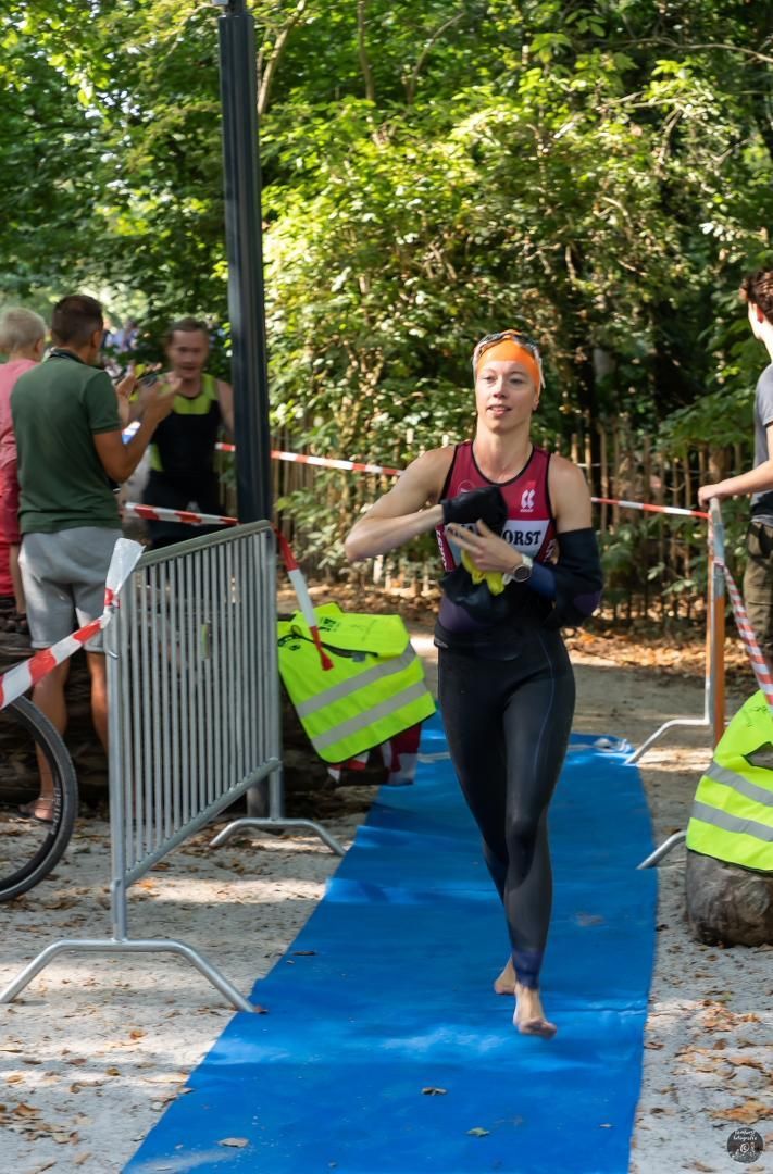 Een vrouw in een wetsuit loopt over een blauwe loper.