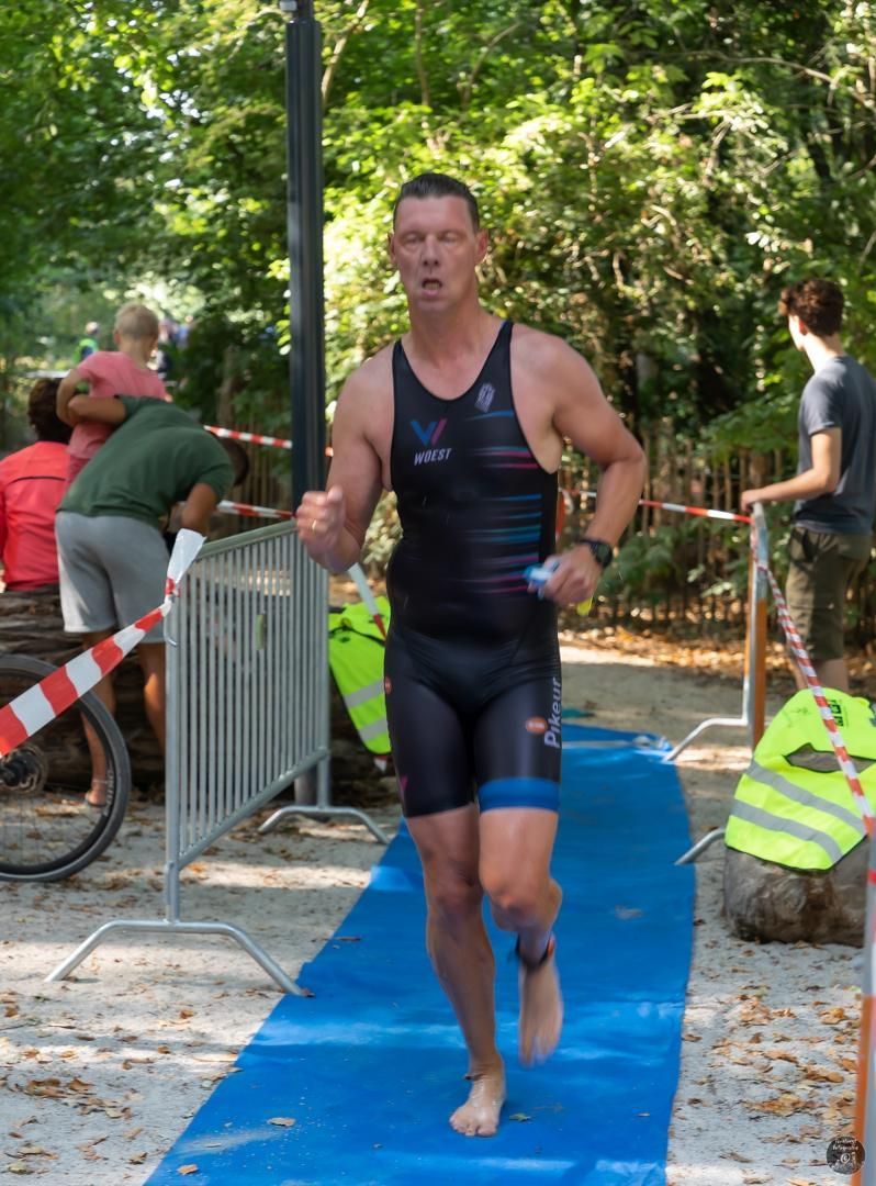 Een man in een zwart tanktopje en korte broek rent op een blauwe mat