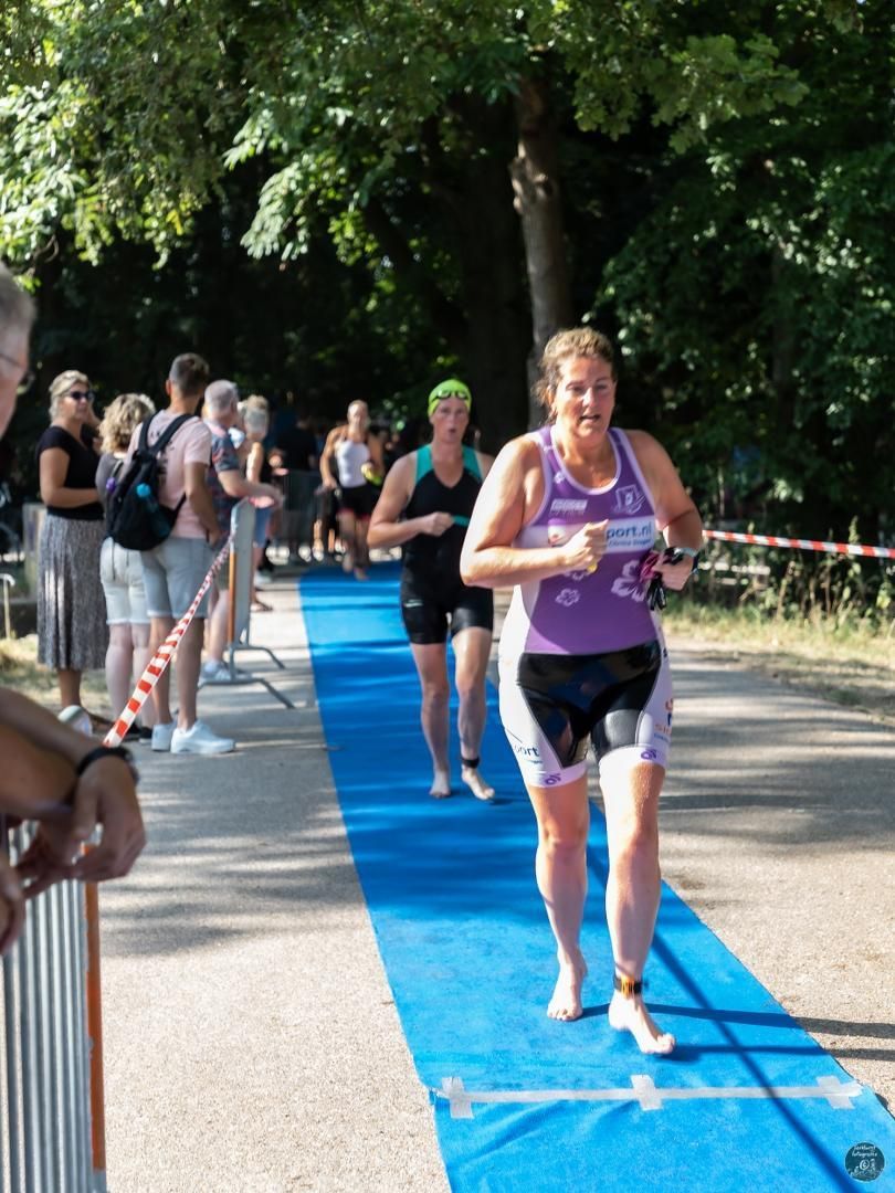 Een vrouw in een paars shirt rent over een blauwe loper.