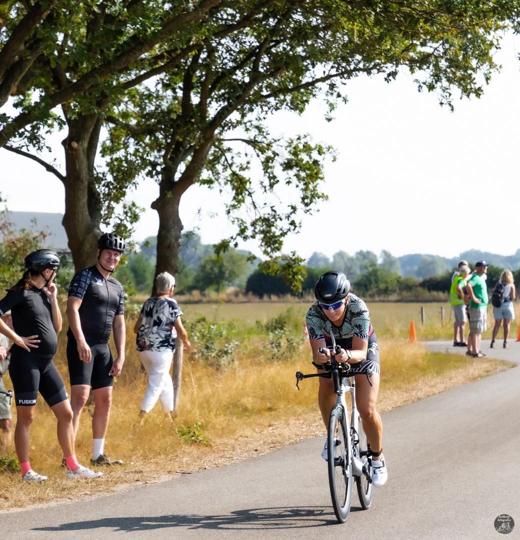 Een man die op een fiets over een weg rijdt terwijl mensen toekijken