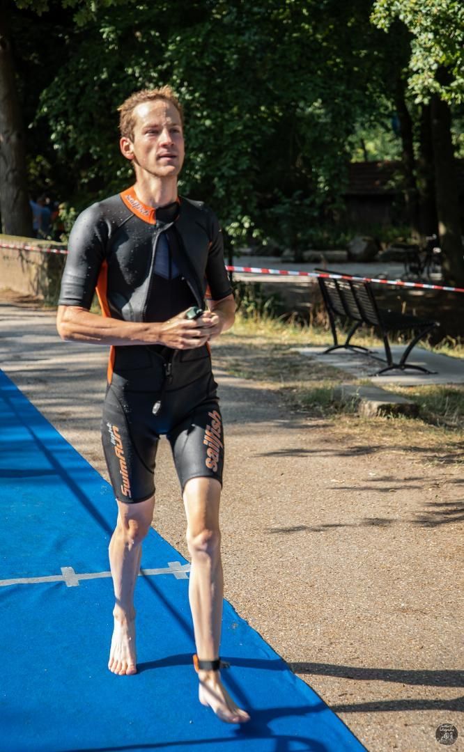 Een man in een wetsuit rent op een blauwe baan.