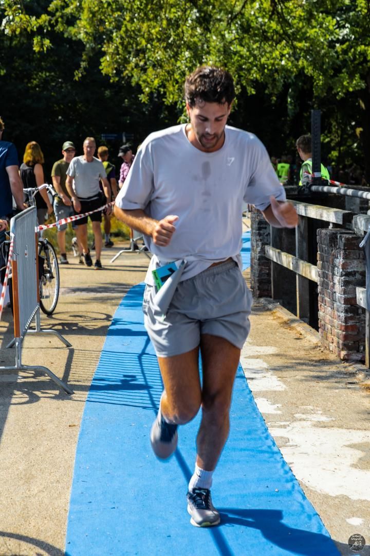 Een man in een wit overhemd en een grijze korte broek rent over een blauwe loper.