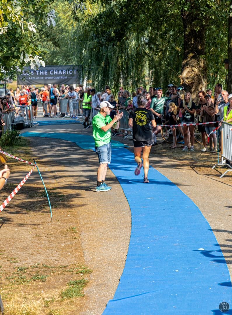 Een vrouw rent op een blauw pad voor een menigte mensen.