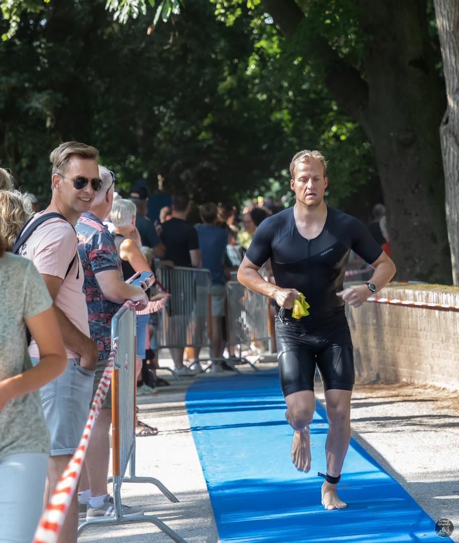 Een man rent op blote voeten op een blauwe mat voor een menigte mensen.