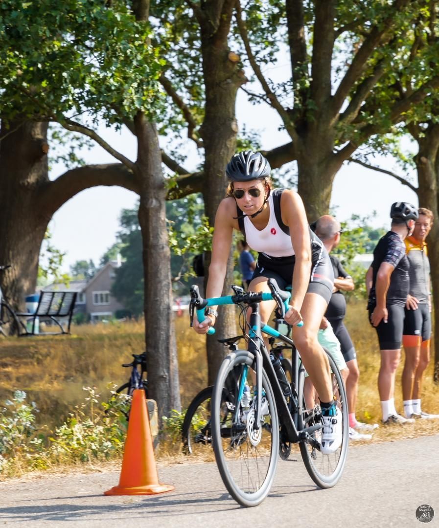 Een vrouw fietst over een weg naast een oranje kegel