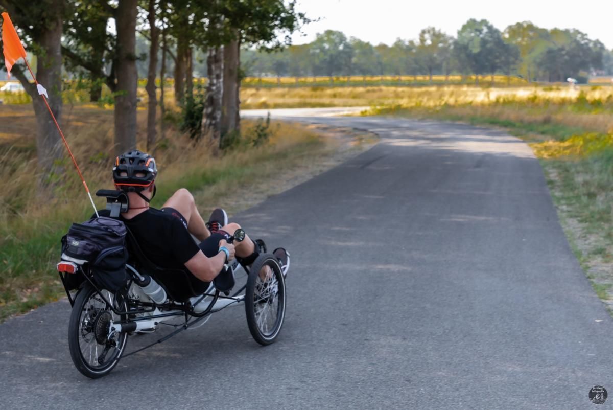 Een man rijdt op een ligfiets over een weg