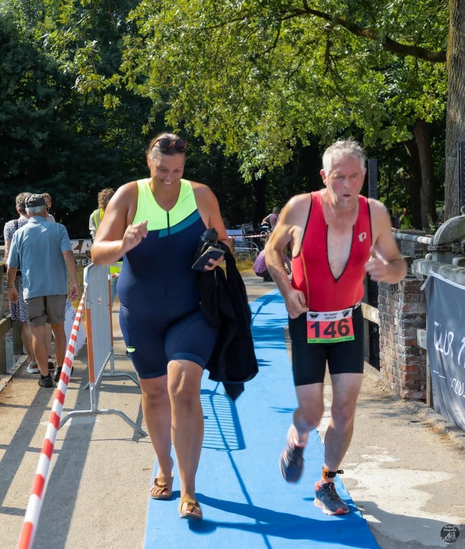 Een man in een rood tanktopje met het nummer 146 op zijn middel rent met een vrouw