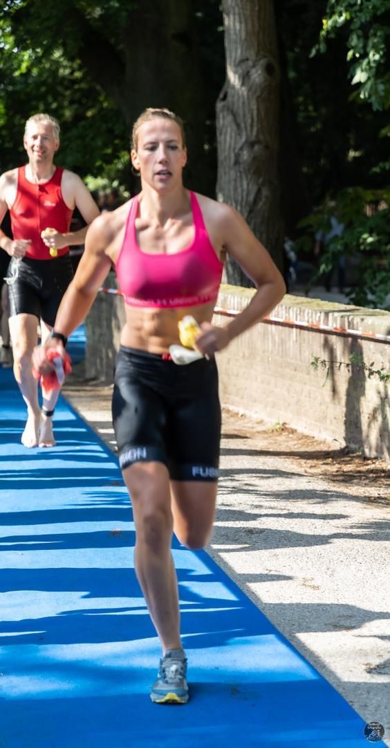 Een vrouw in een roze topje en een zwarte korte broek rent op een blauwe baan.