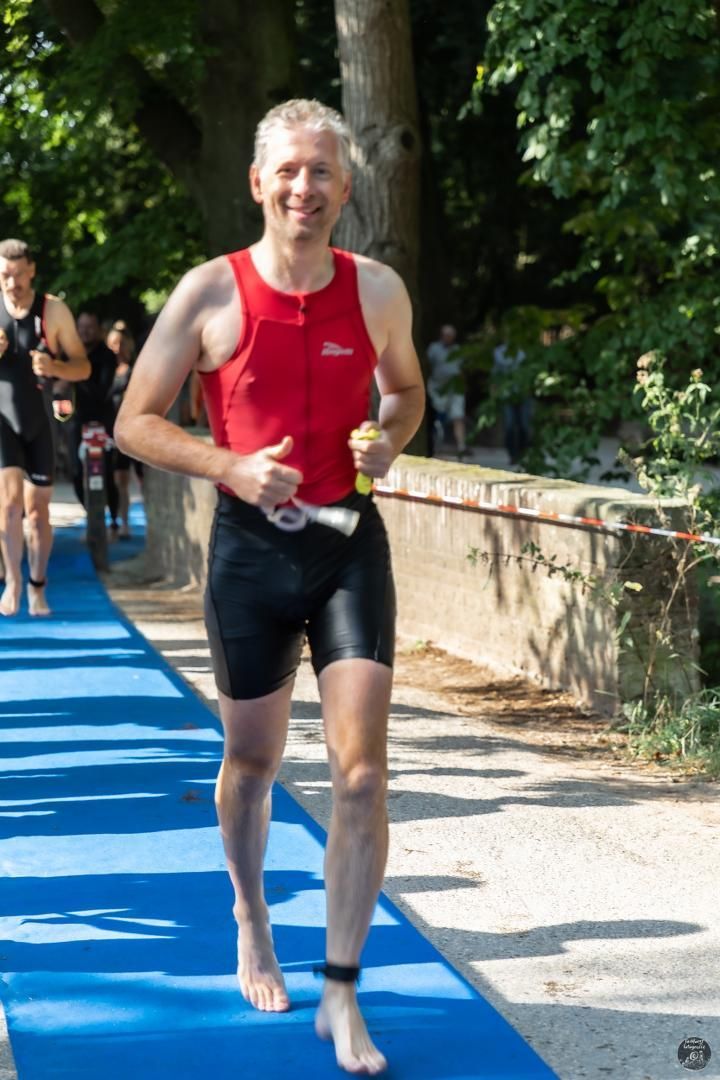 Een man in een rood tanktopje en een zwarte korte broek rent op een blauwe mat.