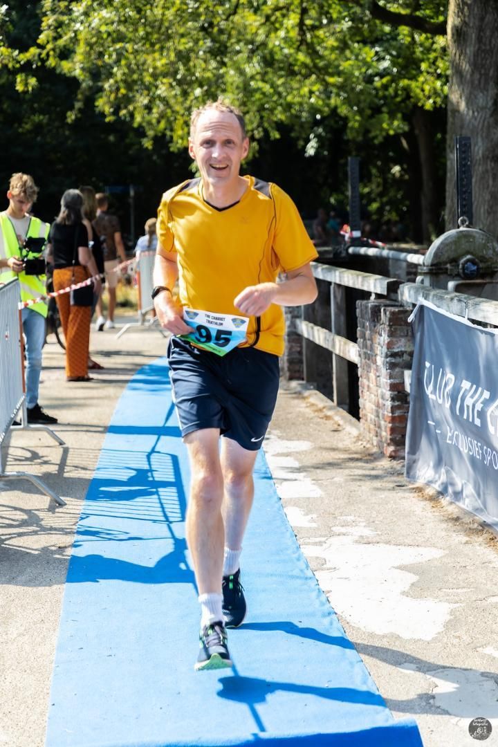 Een man in een geel shirt rent over een blauwe loper.