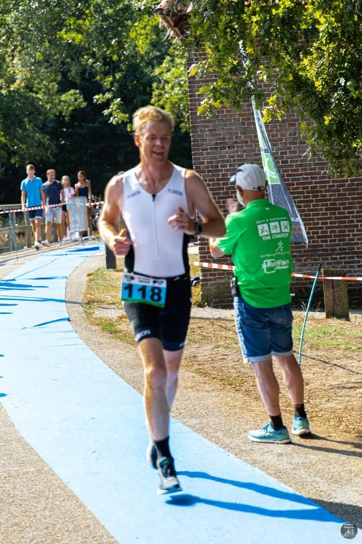 Een man in een wit tanktopje en een zwarte korte broek rent op een blauwe baan.