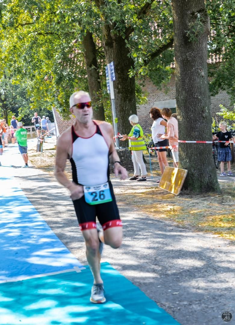 Een man rent mee in een triatlon met nummer 26 op zijn startnummer.