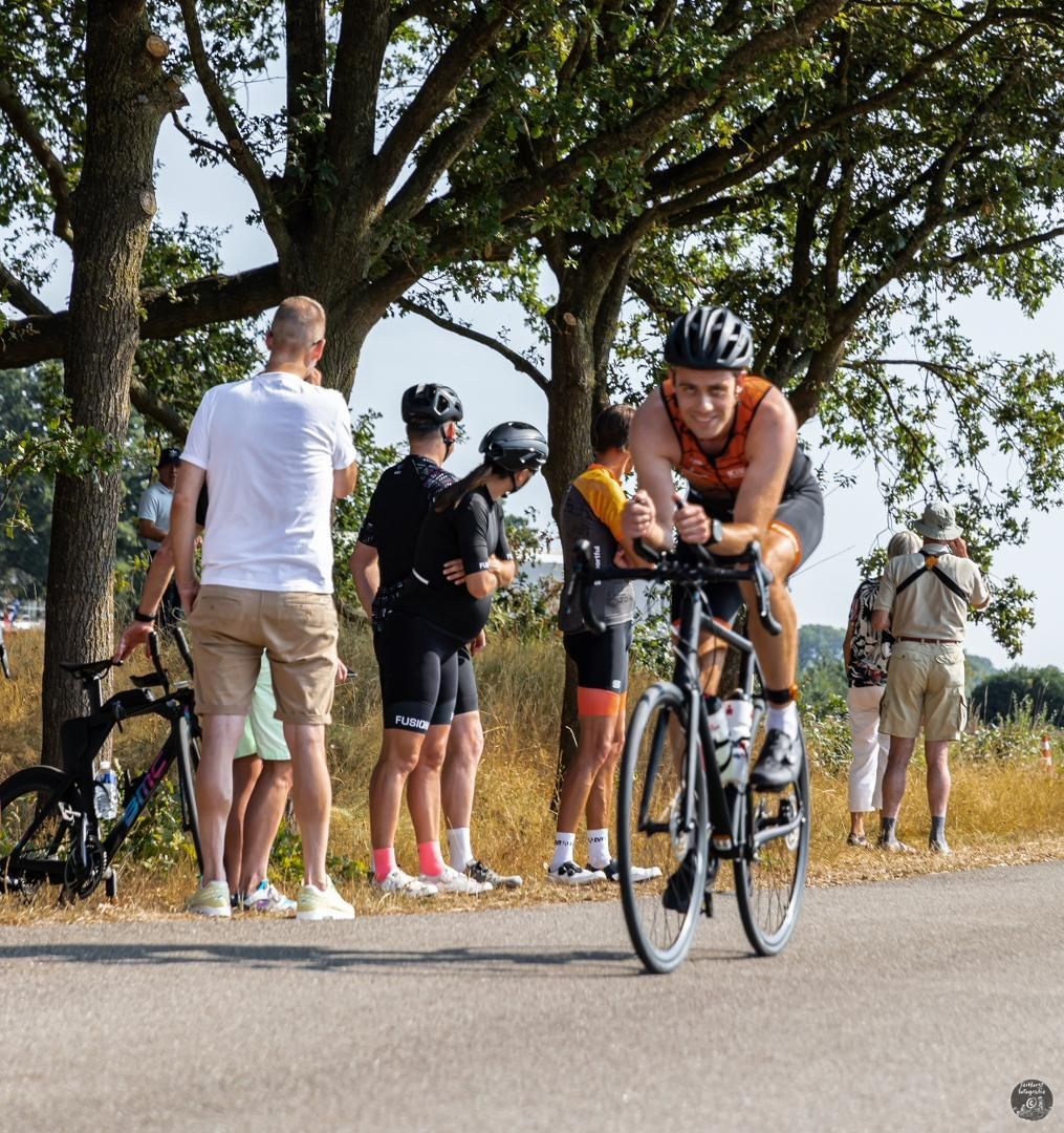 Een groep mensen kijkt naar een man die op een fiets over een weg rijdt
