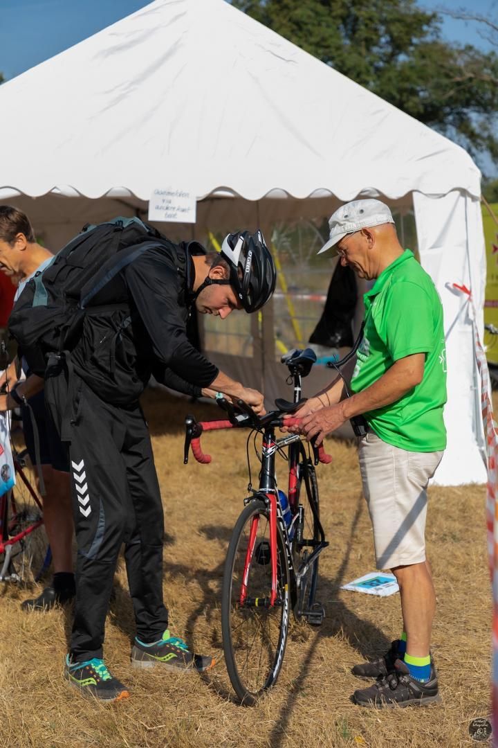 Een man in een groen shirt helpt een andere man met het repareren van een fiets.