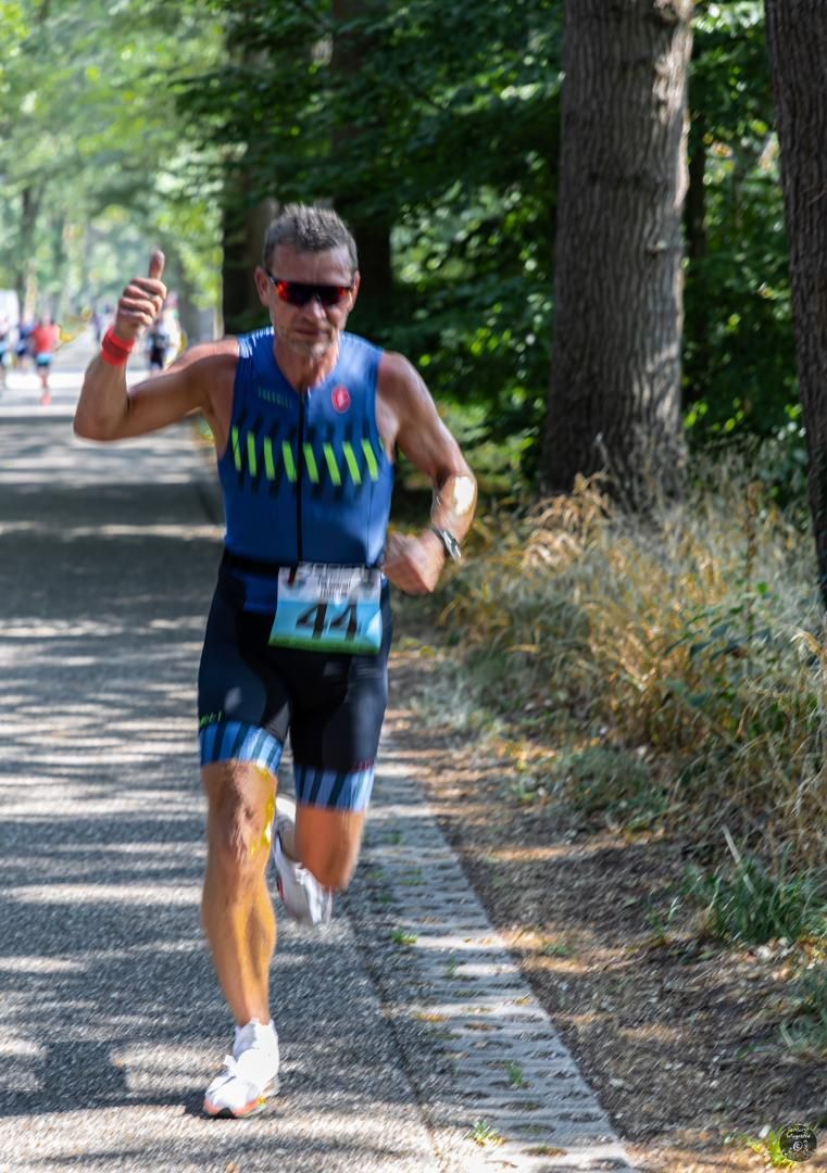 Een man in een blauw tanktopje en een zwarte korte broek rent over een pad.