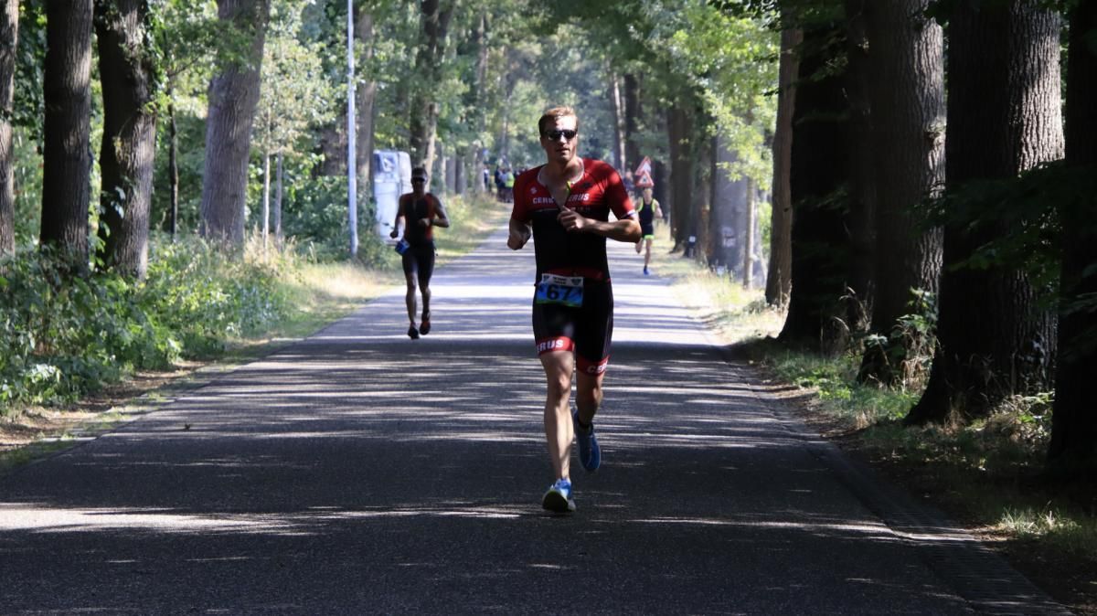 Een man rent over een weg die omgeven is door bomen.