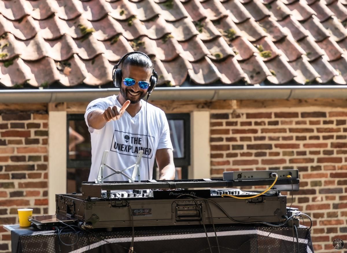 Een man met een koptelefoon en een zonnebril speelt muziek voor een bakstenen gebouw.