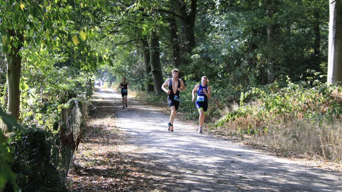 Twee mensen rennen over een onverharde weg in het bos.
